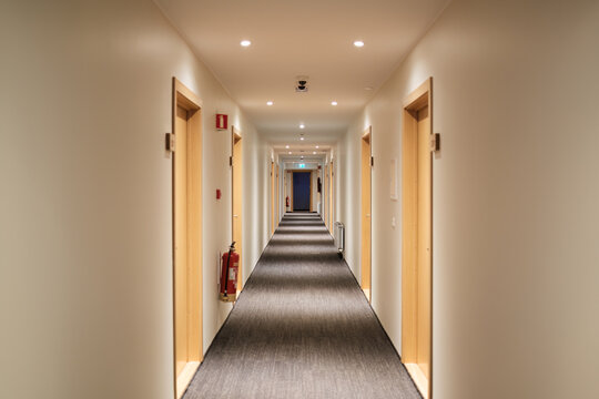 Emptry hotel corridor with carpet floor, wooden doors, fire extinguisher and emergency exit sign