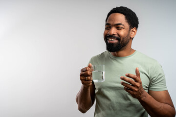 Young Black man drinking fresh water from glass, standing isolated in studio background, copy space. Healthy lifestyle a man drinking water.