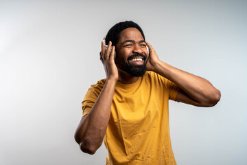 Handsome Blackman with cellphone listening to music in headphones, singing along to his favorite song on grey studio background.