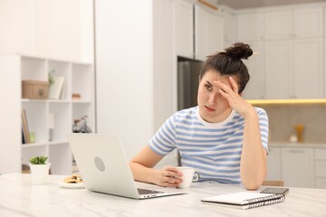 Fototapeta premium Tired woman with cup and laptop at white marble desk in home office. Space for text