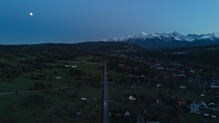 Scenic road leading to snowy mountains under full moon at dusk