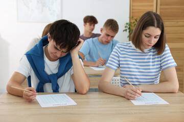 Students taking exam at wooden table indoors