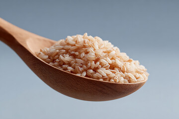 Brown rice grains in a wooden spoon against a soft blue background