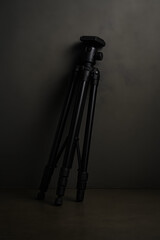 Tripod Leaning: A sleek black tripod leans gracefully, set against a muted background, perfect for capturing professional imagery.