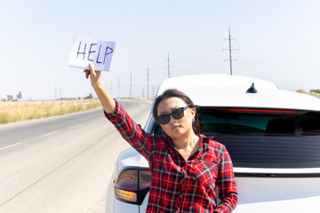 woman is standing on the side of a road next to her car,holding up a sign HELP