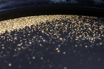 Closeup view of gold flakes collected in a black panning pan. Shiny metallic particles representing mining, prospecting, natural resources, and the search for wealth and treasure.