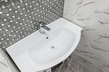 crisp, clean bathroom sink with chrome faucet is surrounded by grey-toned tiles. The patterned walls add texture