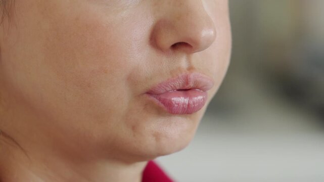 A close-up captures a woman with pursed lips, exhaling air from her mouth. Her action suggests an emotion like exasperation, relief, or a deliberate breath.