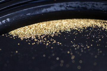 Closeup view of gold flakes collected in a black panning pan. Shiny metallic particles representing mining, prospecting, natural resources, and the search for wealth and treasure.