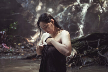 Serene Moment of a Woman in Nature Near Waterfall Adjusting Her Garment in a Tranquil Forest Setting with Soft Mist and Lush Greenery Surroundings