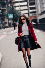 Obraz premium Elegant businesswoman walking through the city streets in high fashion attire, showcasing stylish autumn outerwear and chic urban flair.