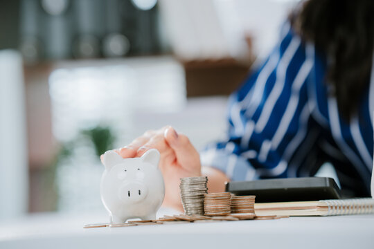 A person in business attire places a coin into a piggy bank beside a laptop, symbolizing saving money and financial management.