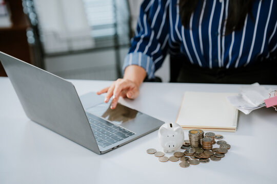 A person in business attire places a coin into a piggy bank beside a laptop, symbolizing saving money and financial management.