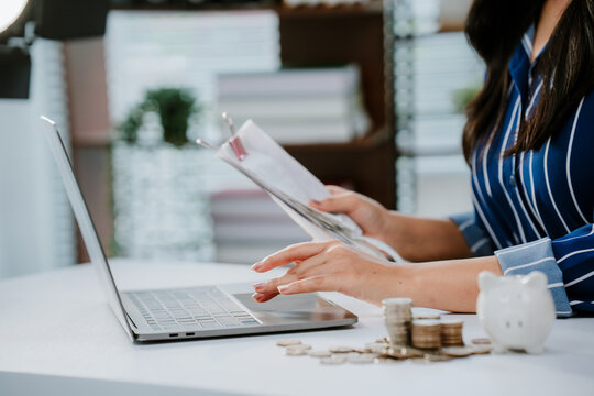 A person in business attire places a coin into a piggy bank beside a laptop, symbolizing saving money and financial management.