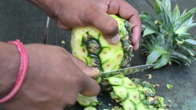 Peeling a Pineapple or Ananas comosus with knife. It is a&nbsp;tropical plant&nbsp;with an edible fruit. It is plant in the family&nbsp;Bromeliaceae. Fruit peeling.
