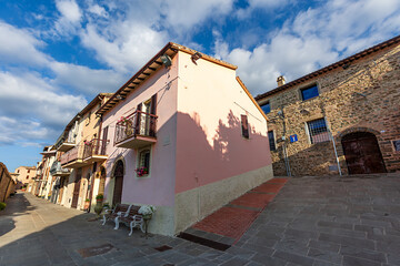 A quiet medieval street in Assisi, Umbria, featuring charming pastel buildings and cobblestone paths under a bright blue sky.