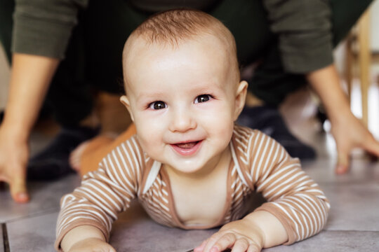 Happy, laughing baby lying on tiled floor at home with no face father on background. Dad And Toddler Child Enjoying Spending Time Together, Cheerful active infant smiling, learning to crawl, playing