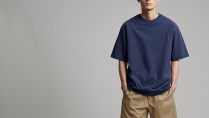 Young man wearing a loose dark blue t shirt and tan shorts against a plain background