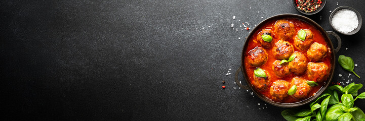 Meatballs in tomato sauce in iron plate on black background.