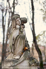 Old cemetery monument of sad mother and baby angel, nature autumn background. Beautiful grieving...