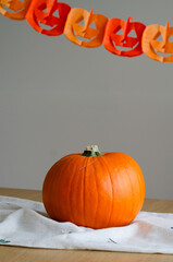 Minimal halloween decor with pumpkin on linen fabric and paper garland in background