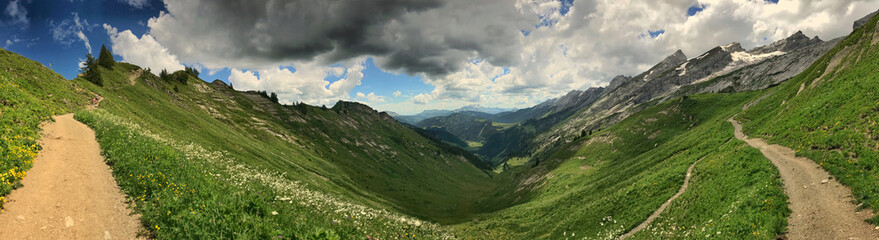 Scenic mountain panorama with lush green valley pathways under dynamic cloudy skies