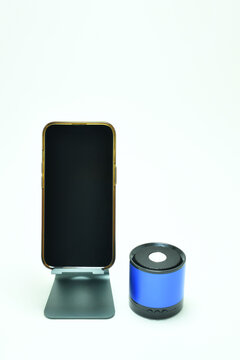 Tel&eacute;fono m&oacute;vil sobre una base de metal, al lado una bocina inal&aacute;mbrica sobre un fondo blanco, espacio para texto en la parte superior y pantalla. Toma vertical.