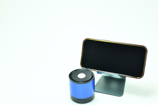 Tel&eacute;fono m&oacute;vil sobre una base de metal, al lado una bocina inal&aacute;mbrica sobre un fondo blanco, espacio para texto al lado izquierdo y pantalla. Toma horizontal