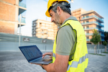 Engineer controlling construction plan on laptop at site