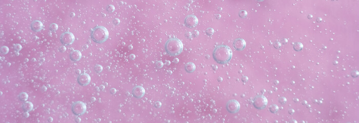 Macro shot of a pastel pink surface covered in different sized transparent bubbles. The composition is soft, airy and minimalistic, offering a playful and dreamy texture for backgrounds
