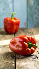Two vibrant red bell peppers resting on a rustic wooden surface, with a blurred teal-toned background