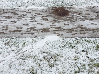 Overhead view of the first thin layer of snow on green grass and footprints across a paved path with a manhole cover concept of early winter, sudden cold weather,