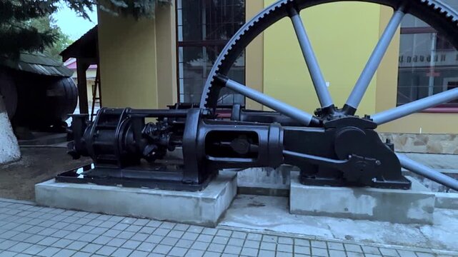 Old black stationary steam engine with a large geared flywheel exhibited outdoors as a monument to industrial history, showcasing intricate mechanical details and engineering from the past era