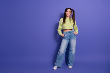 Stylish young woman with trendy casual fashion outfit posing confidently on a purple background...