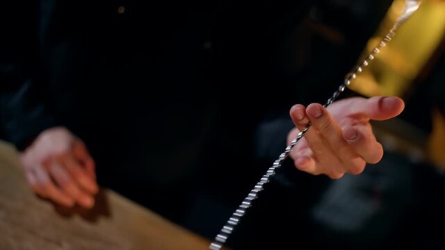 Close-up of hands delicately holding a fine metal chain above a worn wooden workbench in a dimly lit workshop, highlighting jewelry craftsmanship with moody shallow-focus lighting