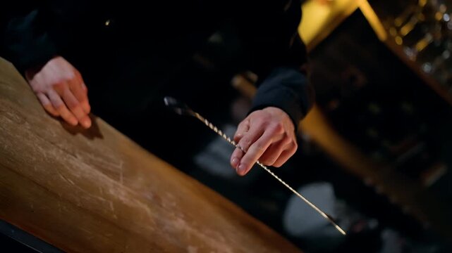 Close-up of hands delicately swinging a metal pendulum on a chain over a worn wooden tabletop in a dim, moody setting, capturing movement, concentration, and ritual divination.