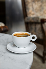A white cup of black coffee americano in a cozy atmosphere of a cafe with copy space
