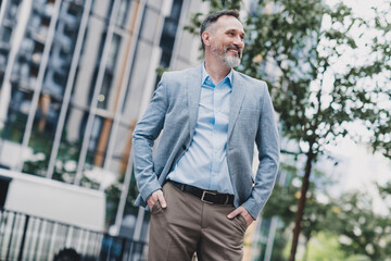 Confident businessman walking in a modern city street wearing a light blue shirt blazer and khaki pants