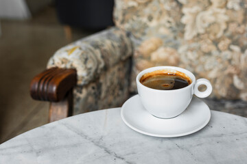 A white cup of black coffee americano in a cozy atmosphere of a cafe with copy space
