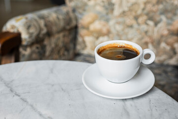 A white cup of black coffee americano in a cozy atmosphere of a cafe with copy space
