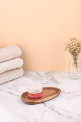 Vertical composition with natural solid shampoos on a wooden tray beside beige towels and a glass vase. Peach background and marble surface. Copy space. Concept of self care and natural cosmetics