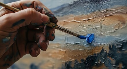 Close-up of an artists hand applying blue paint to a textured canvas with a brush, capturing the creative process of oil painting.