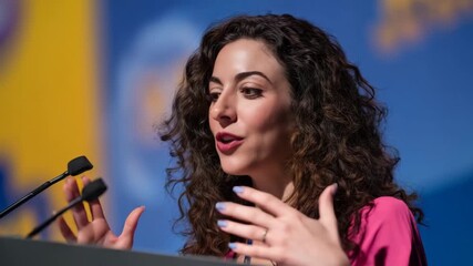 Confident woman giving a speech at a business conference. Professional female speaker presenting from a podium. Public speaking and leadership concept from an animated photograph - Powered by Adobe