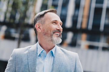 Senior businessman in a modern city looking up with a confident smile wearing a stylish light blue suit for a dynamic professional portrait