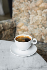 A white cup of black coffee americano in a cozy atmosphere of a cafe with copy space
