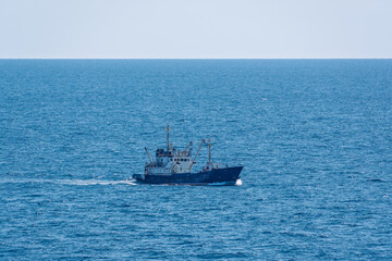 Fototapeta premium Fishing boat in blue sea and clear sky with birds flying overhead.