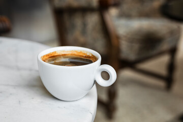 A white cup of black coffee americano in a cozy atmosphere of a cafe with copy space
