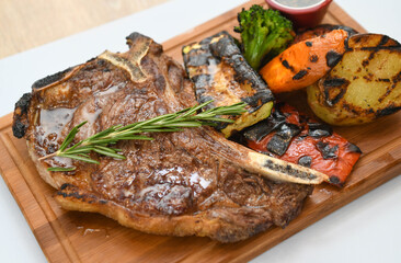 Grilled beef steak with rosemary on a wooden board, served with roasted zucchini and peppers.