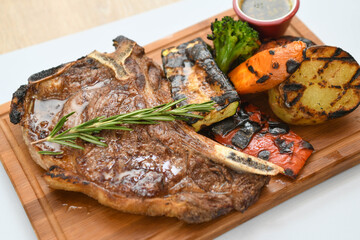 Grilled beef steak with rosemary on a wooden board, served with roasted zucchini and peppers.