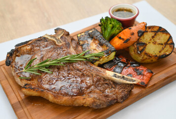 Grilled beef steak with rosemary on a wooden board, served with roasted zucchini and peppers.